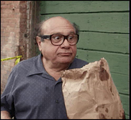 A Bald Man Wearing Glasses Is Holding A Brown Bag GIF