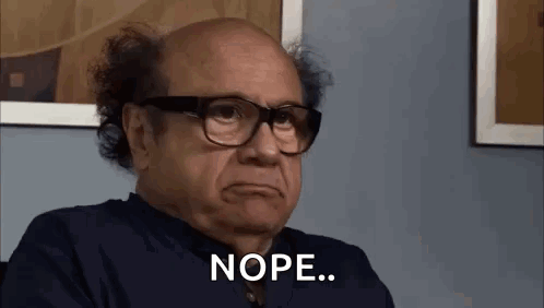 A Bald Man Wearing Glasses Is Sitting In Front Of A Wall And Making A Funny Face . GIF