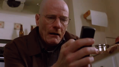 A Bald Man Wearing Glasses Looks At His Cell Phone GIF
