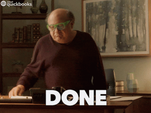 A Bald Man Wearing Green Glasses Is Standing In Front Of A Desk With The Word Done Written On It GIF