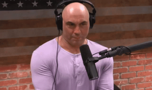 A Bald Man Wearing Headphones And A Purple Shirt Is Sitting In Front Of A Microphone GIF