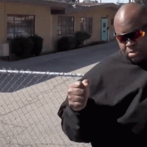 A Bald Man Wearing Sunglasses And A Black Shirt Is Pointing At The Camera GIF