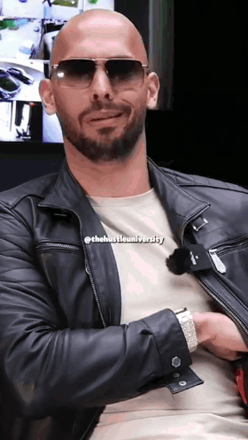 A Bald Man Wearing Sunglasses And A Leather Jacket With The Hustle University Written On His Shirt GIF