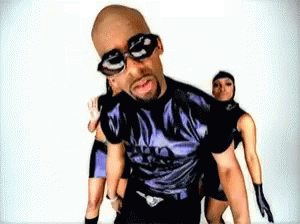 A Bald Man Wearing Sunglasses And A Purple Shirt Is Surrounded By Three Women GIF