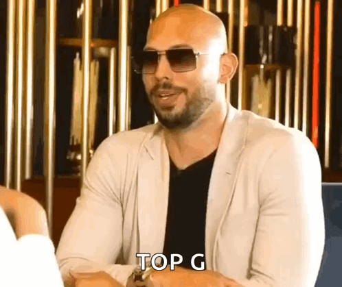 A Bald Man Wearing Sunglasses Is Sitting At A Table And Says Top G . GIF