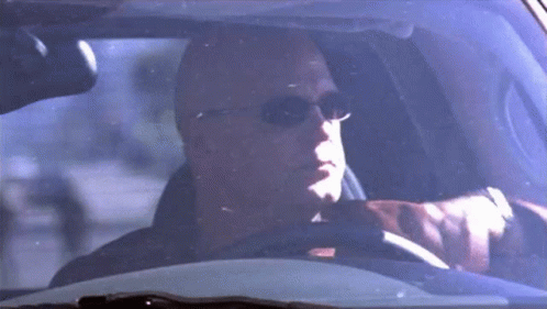 A Bald Man Wearing Sunglasses Is Sitting In A Car . GIF