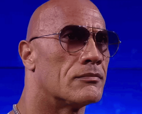 A Bald Man Wearing Sunglasses Looks At The Camera GIF