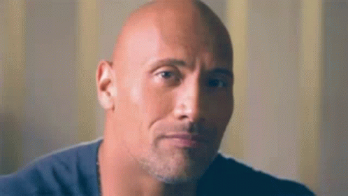A Bald Man With A Beard And A Blue Shirt Is Looking At The Camera . GIF