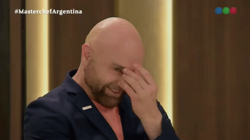 A Bald Man With A Beard Is Covering His Face In Front Of A Masterchef Argentina Logo GIF