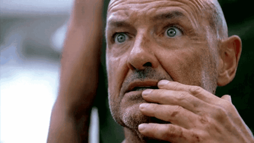 A Bald Man With A Beard Is Covering His Mouth With His Hands GIF