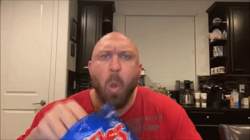 A Bald Man With A Beard Is Eating A Bag Of Lays Chips GIF
