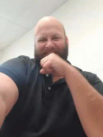 a bald man with a beard is holding his fist up in the air while wearing a black shirt .