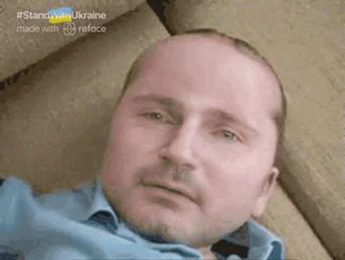 A Bald Man With A Beard Is Laying Down On A Couch . GIF