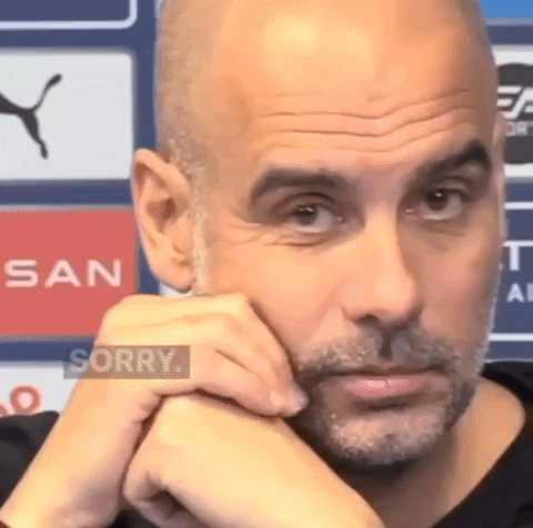 A Bald Man With A Beard Is Sitting With His Hands On His Chin And Looking At The Camera . GIF