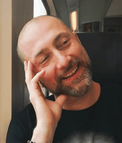 A Bald Man With A Beard Is Smiling With His Hand On His Face GIF