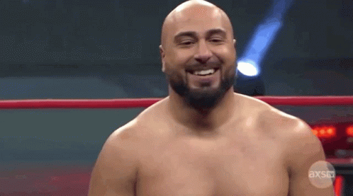A Bald Man With A Beard Is Standing In A Wrestling Ring Smiling . GIF