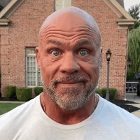A Bald Man With A Beard Is Standing In Front Of A Brick House And Making A Funny Face . GIF