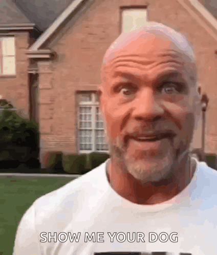 a bald man with a beard is standing in front of a brick house and saying show me your dog .