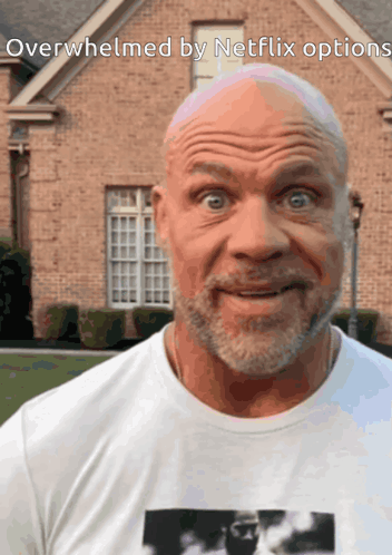 A Bald Man With A Beard Is Standing In Front Of A Brick House With The Words Overwhelmed By Netflix Options Below Him GIF