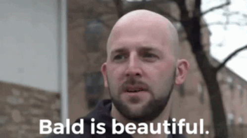 A Bald Man With A Beard Is Standing In Front Of A Building And Says Bald Is Beautiful GIF