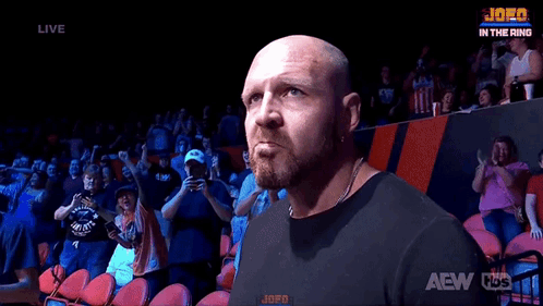 A Bald Man With A Beard Is Standing In Front Of A Crowd In A Stadium . GIF
