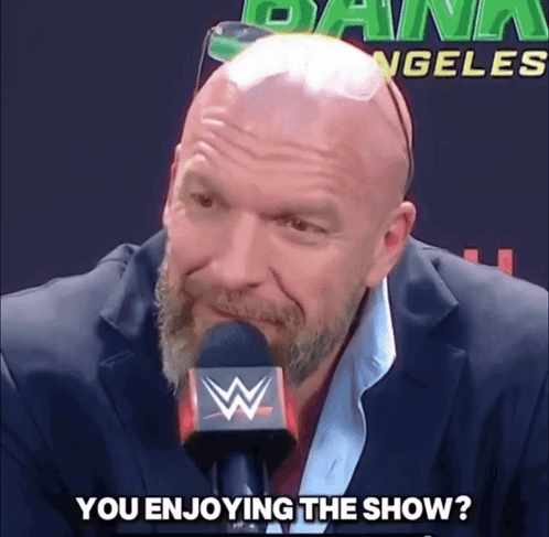 a bald man with a beard is talking into a microphone with the words " you enjoying the show " written below him