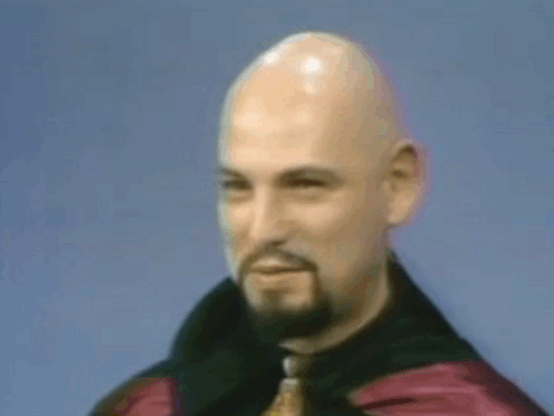 A Bald Man With A Beard Is Wearing A Black Jacket And Tie GIF
