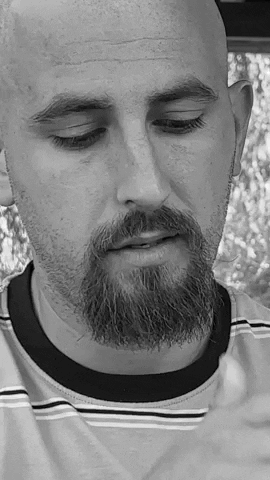 a bald man with a beard is wearing a striped shirt and has his eyes closed .