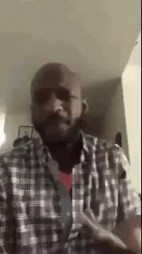 A Bald Man With A Beard Wearing A Plaid Shirt Is Standing In A Living Room . GIF