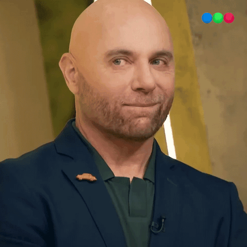 a bald man with a beard wears a blue suit