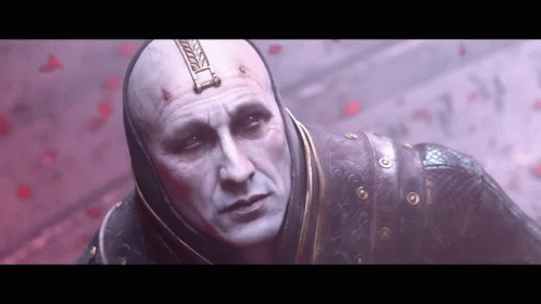 A Bald Man With A Hood On His Head Is Standing In Front Of A Red Wall . GIF
