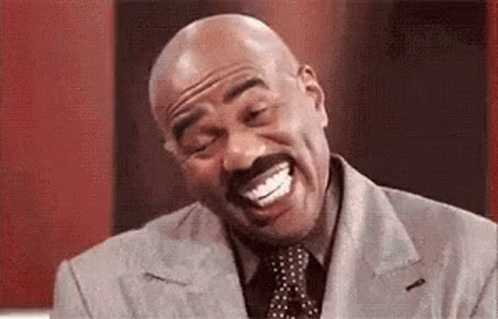 A Bald Man With A Mustache Is Laughing With His Mouth Open While Wearing A Suit And Tie . GIF