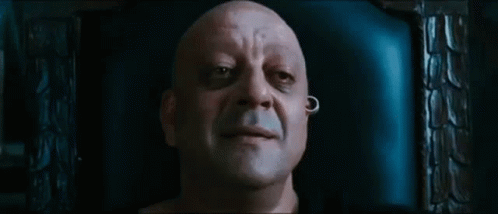 A Bald Man With A Piercing In His Ear Is Sitting In A Chair And Smiling . GIF