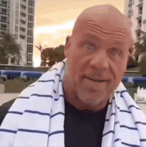 A Bald Man With A Striped Towel Around His Neck Looks At The Camera GIF
