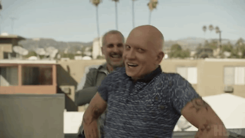 a bald man with a tattoo on his arm is standing next to another bald man .