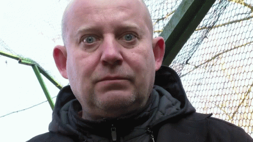 A Bald Man With Blue Eyes And A Beard Wears A Black Jacket GIF