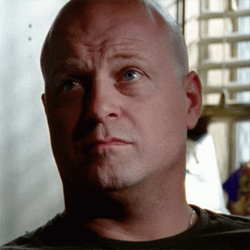 A Bald Man With Blue Eyes Looks At The Camera With A Serious Look On His Face GIF