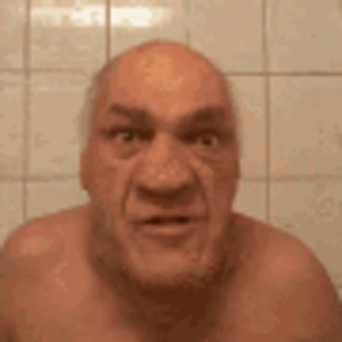 a bald man without a shirt is making a funny face while standing in front of a tiled wall .