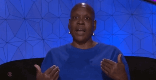 Bald Woman In Blue Shirt Sitting With Outstretched Hands GIF