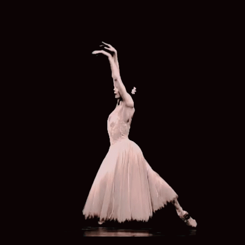 A Ballerina In A White Dress And Pointe Shoes Is Dancing In The Dark GIF