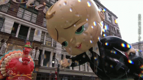 A Balloon Of A Baby In A Suit Is Floating In Front Of A Building That Says Macy 'S GIF
