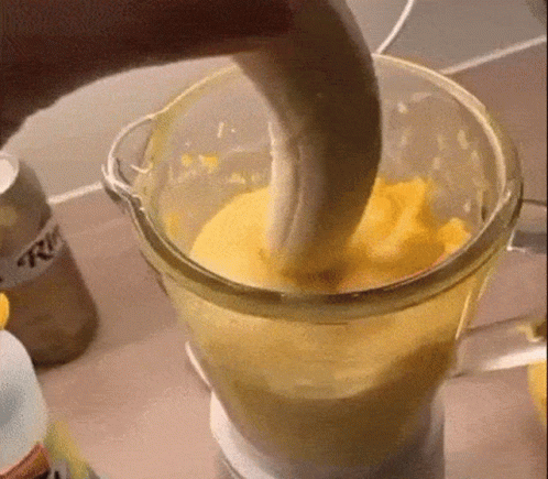 A Banana Is Being Added To A Blender Filled With Yellow Liquid . GIF