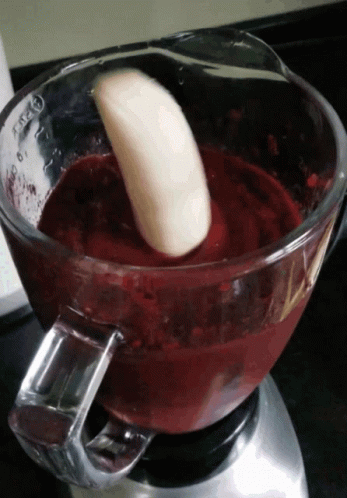 A Banana Is Being Added To A Blender With A Red Liquid GIF