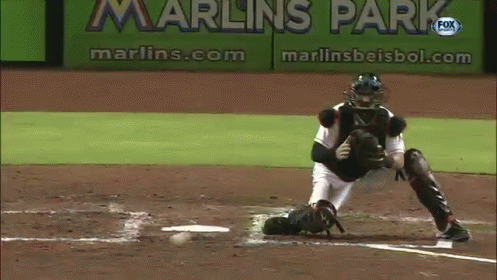 A Baseball Player Catches A Ball In Front Of A Sign That Says Marlins Park GIF