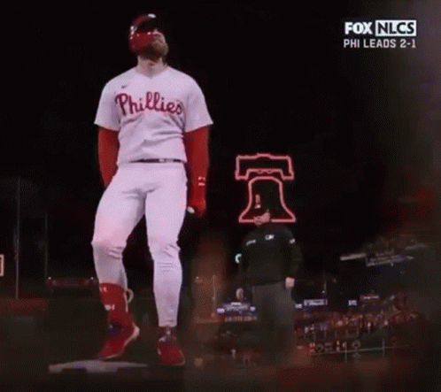A Baseball Player In A Phillies Uniform Is Standing On A Mound In Front Of A Bell Sign . GIF