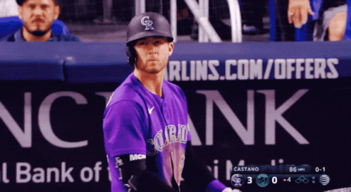 A Baseball Player In A Purple Uniform Stands In Front Of A Bank Of America Sign GIF