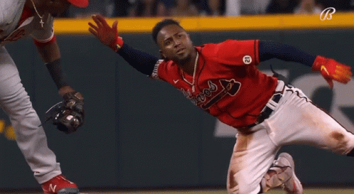 A Baseball Player In A Red Braves Jersey Is Sliding Into Base GIF