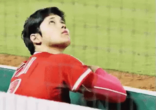 A Baseball Player In A Red Uniform Is Sitting In The Dugout Looking Up . GIF