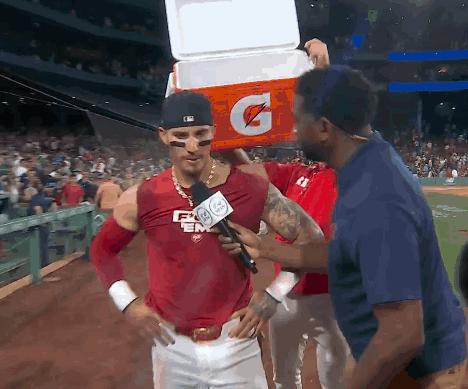 a baseball player is being interviewed by a reporter while holding a gatorade cooler on his head