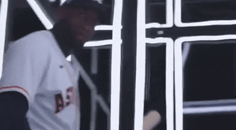 A Baseball Player Is Holding A Bat In A Dark Room . GIF